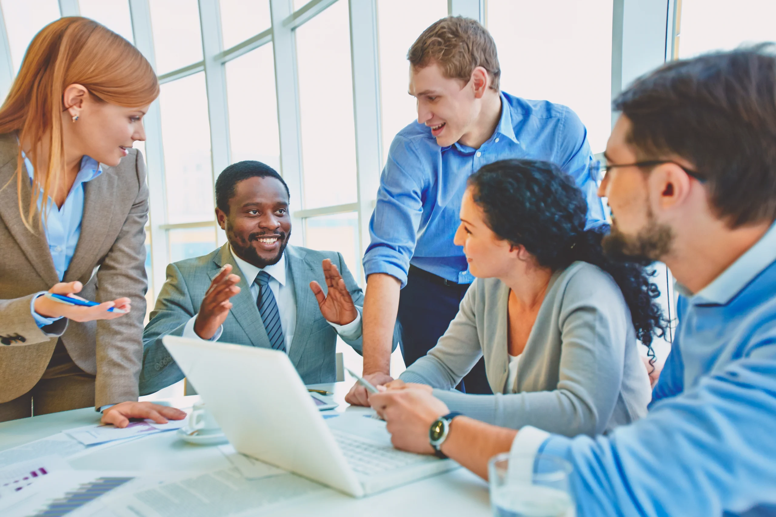 A group of five business professionals actively discussing an idea in an office meeting.