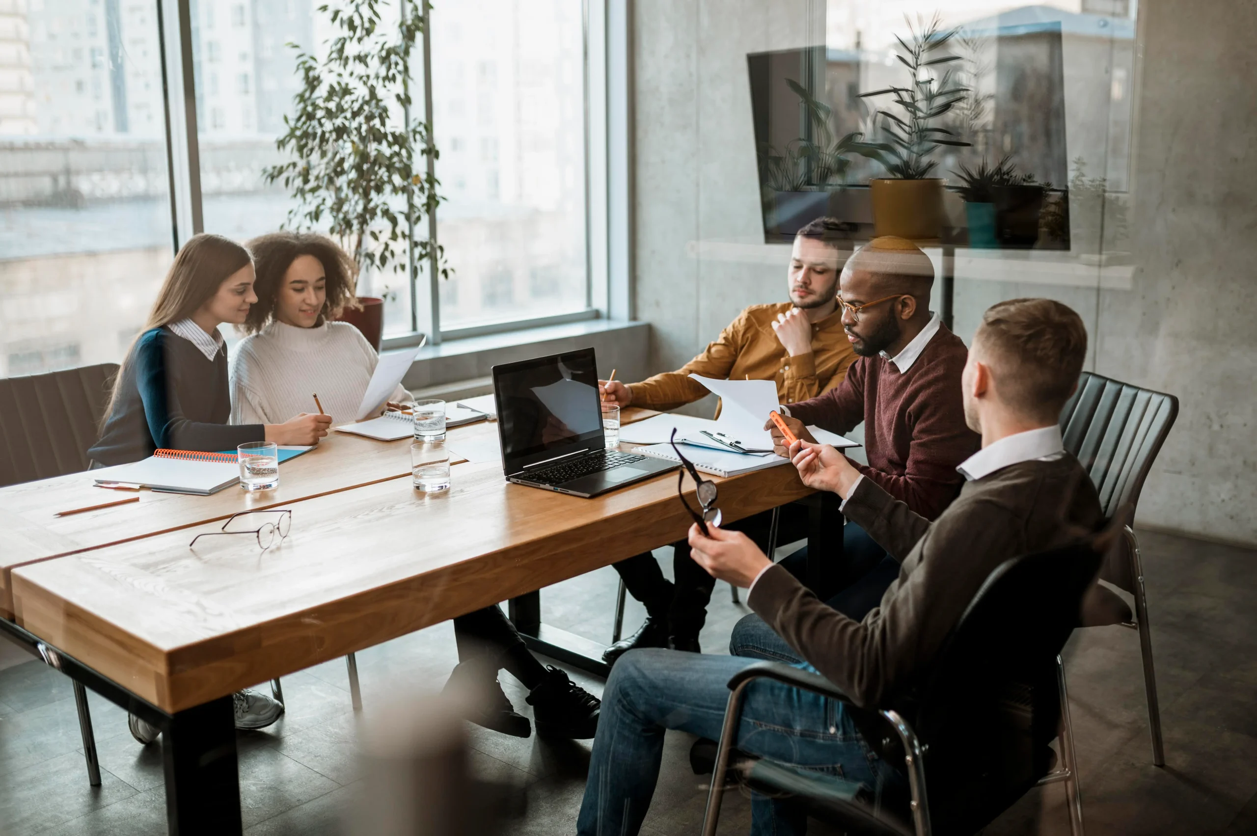 Group of people sitting around a conference table in a modern office, collaborating on documents and working with a laptop during a team meeting.