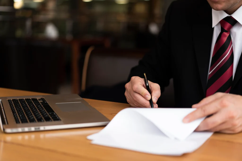 Business professional reviewing and signing documents beside a laptop, representing digital transformation and automation in the insurance industry.