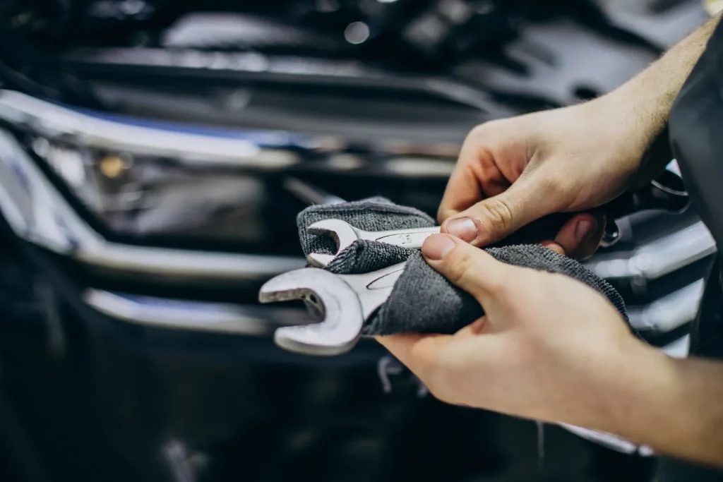 Close-up of hands wiping two wrenches with a grey rag near the front of a car.