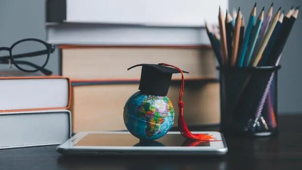 Global Education and Study Abroad Concept: Small globe with a graduation cap on a tablet, surrounded by books and pencils.
